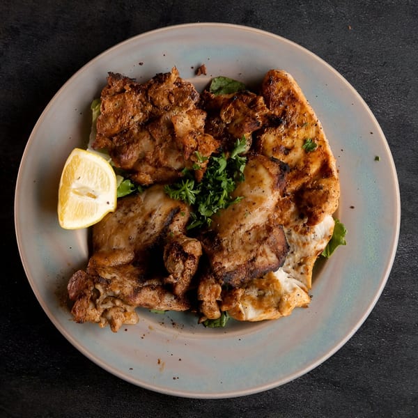 Grilled chicken pieces with fresh parsley and a lemon wedge on a light blue plate.