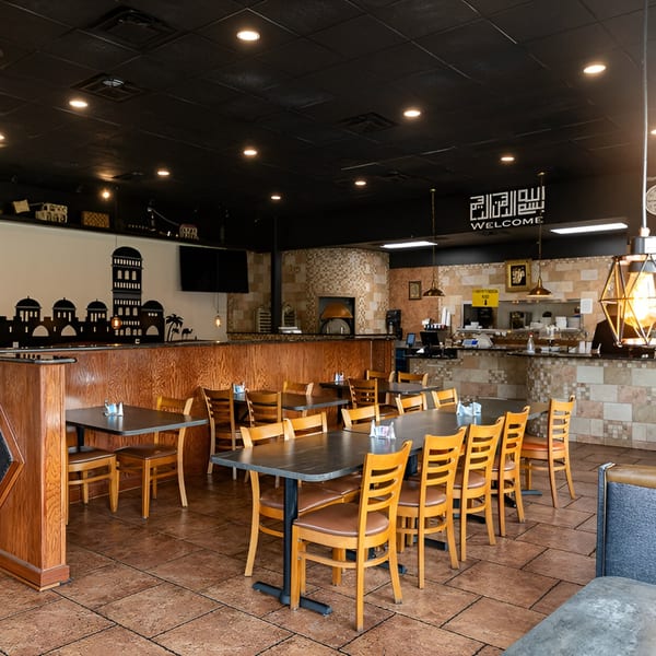 La Marra's dining room with wooden tables and chairs, a large pizza oven, and Middle Eastern decor.