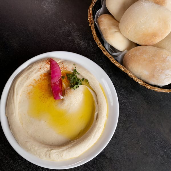 Creamy hummus with olive oil, parsley, and pickled turnip, served with a basket of pita bread.