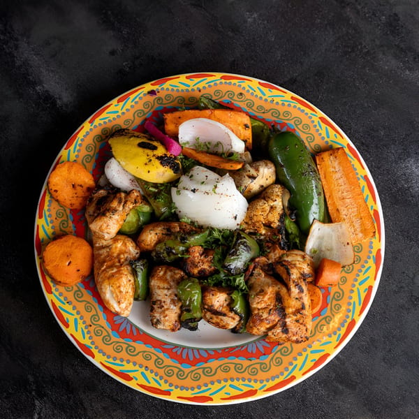 Grilled chicken and vegetables, including bell peppers, onions, and carrots, on a colorful plate.